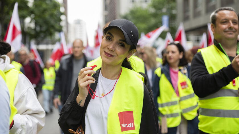 ver.di-Aktive mit gelben Warnwesten bei einer Demonstration, eine Frau mit Trillerpfeife im Vordergrund