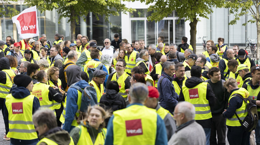 Foto einer ver.di-Streiksituation bei der die Leute gelbe Warnwesten tragen und ver.di-Flaggen schwenken