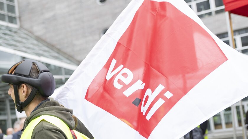Foto auf dem eine Person mit Radhelm eine große ver.di-Flagge auf der Schulter trägt