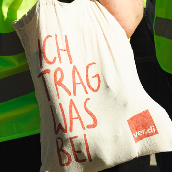 ver.di-Stoffbeutel, den jemand trägt, auf dem steht "Ich trag was bei"