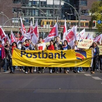 Demonstrationszug mit Postbank-Banner und ver.di-Flaggen