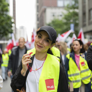ver.di-Aktive mit gelben Warnwesten bei einer Demonstration, eine Frau mit Trillerpfeife im Vordergrund