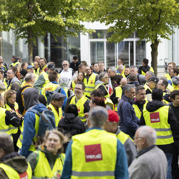 Foto einer ver.di-Streiksituation bei der die Leute gelbe Warnwesten tragen und ver.di-Flaggen schwenken