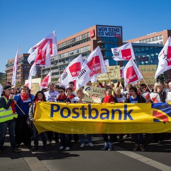 Demonstrationszug mit Postbank-Banner und ver.di-Flaggen