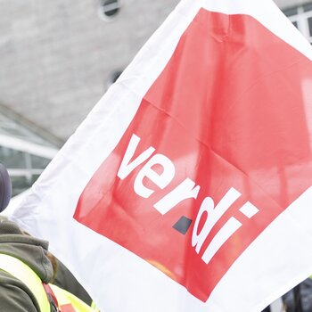 Foto auf dem eine Person mit Radhelm eine große ver.di-Flagge auf der Schulter trägt