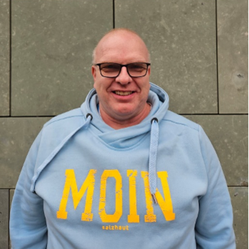 Dirk Sievers ein Mann mit Brille und Pullover auf dem "Moin" steht