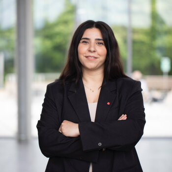 Kübra Kyei, eine junge Frau mit schwarzem Blazer und verschränken Armen blickt direkt in die Kamera.